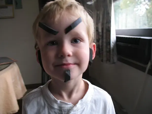 Portrait of Scott Stilson’s son with pieces of black weatherstrip affixed to his face as ersatz facial hair