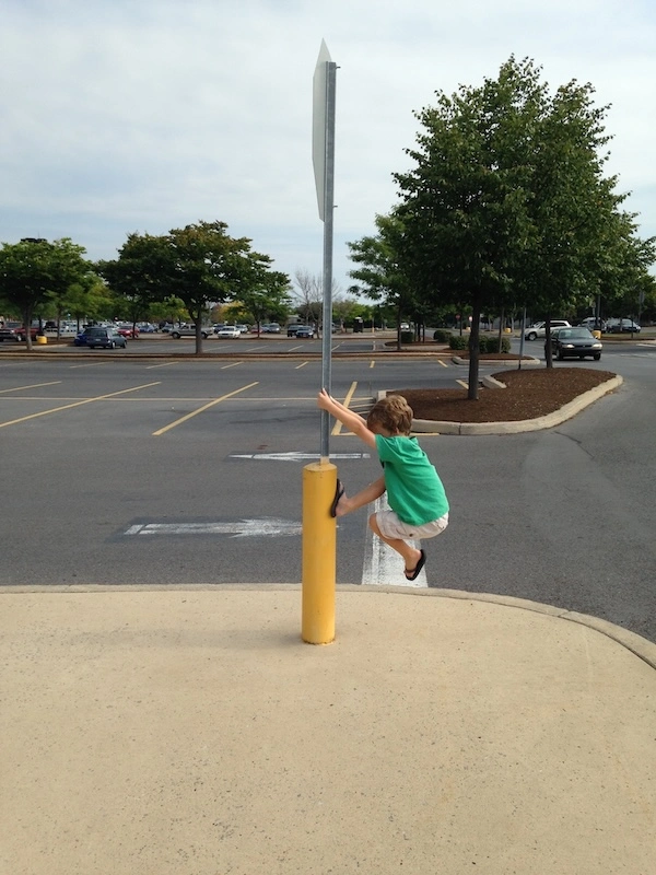 A child is playfully climbing a stop sign pole near a parking lot